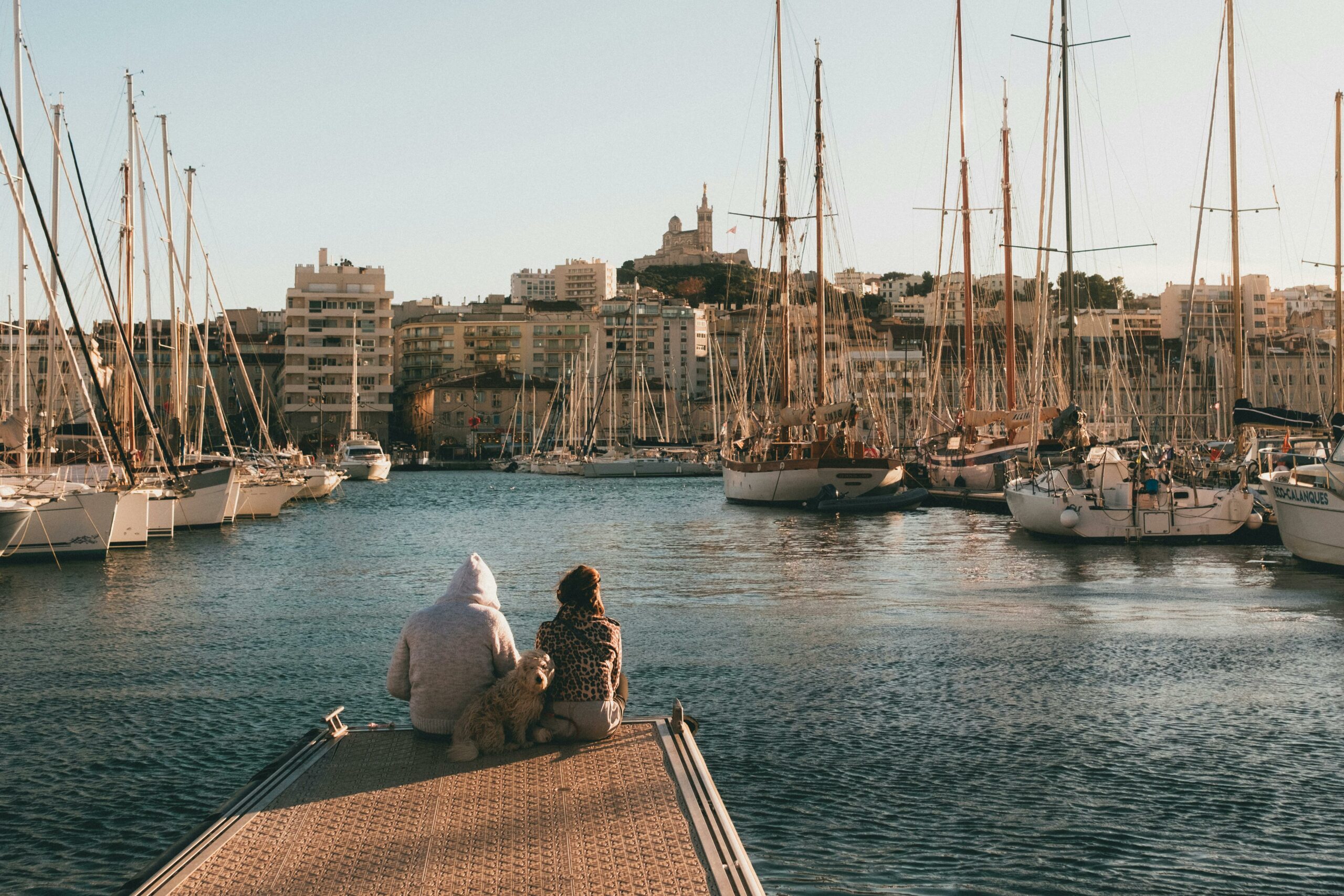 Couple and dog relaxing by the harbor with Marseille skyline.