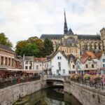 Charming view of Amiens Cathedral rising above a picturesque canal and historic houses.