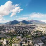 A breathtaking aerial view captures a vibrant city nestled between majestic mountains under a clear blue sky.