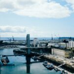 A vibrant urban cityscape with modern architecture and a bustling harbor under a cloudy sky.