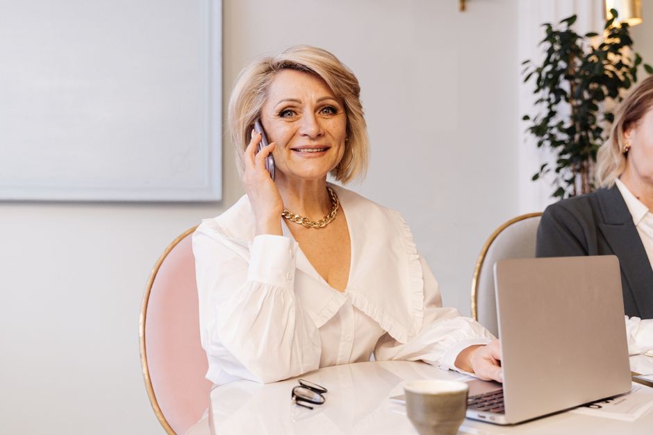 Une femme senior souriante en blouse blanche parlant au téléphone tout en travaillant dans un environnement de bureau moderne.