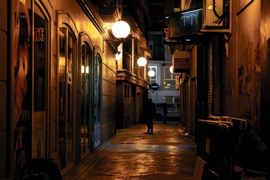 Une allée urbaine sombre et étroite illuminée par des lampadaires chauds la nuit, créant une atmosphère mélancolique.