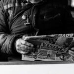Un adulte senior lisant un journal dans un cadre intérieur confortable, capturé en noir et blanc.