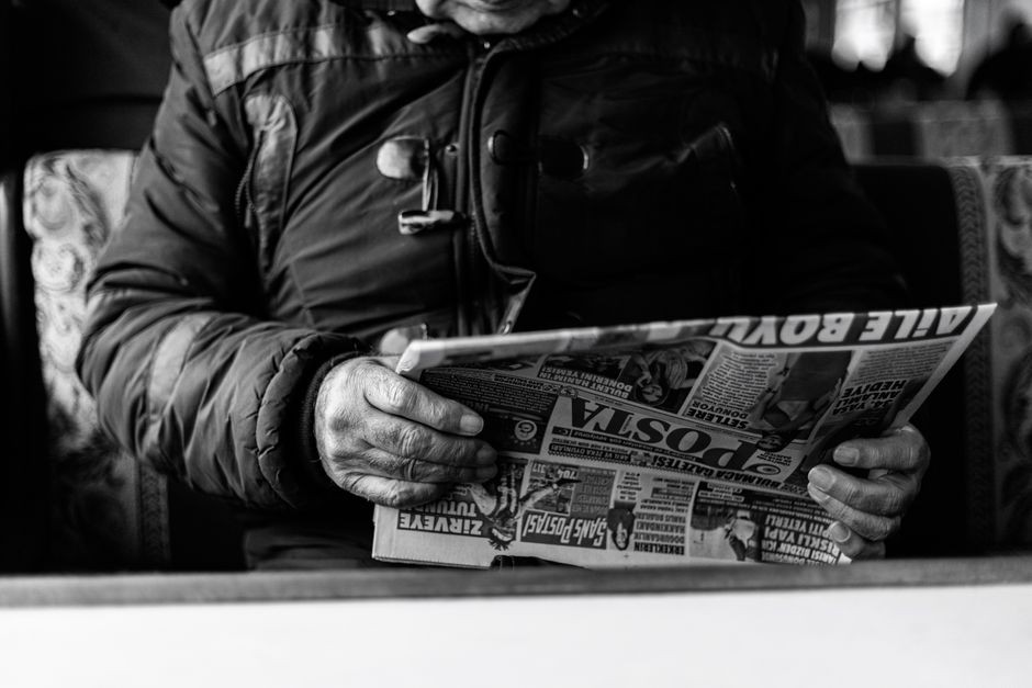 Un adulte senior lisant un journal dans un cadre intérieur confortable, capturé en noir et blanc.